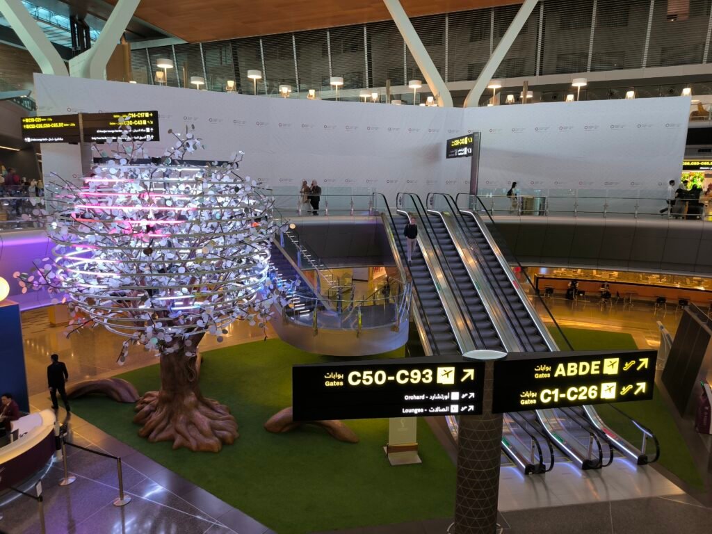 Interior of Hamad International Airport featuring a lighting tree, escalators and signs pointing to gates.
