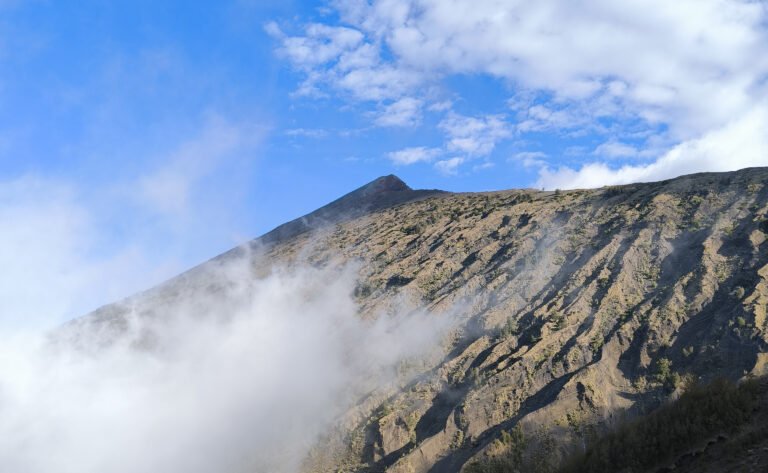 View of Mount Rinjani's summit towering above. The sun highlighting the volcanic terrain along the sides of the crater rim.